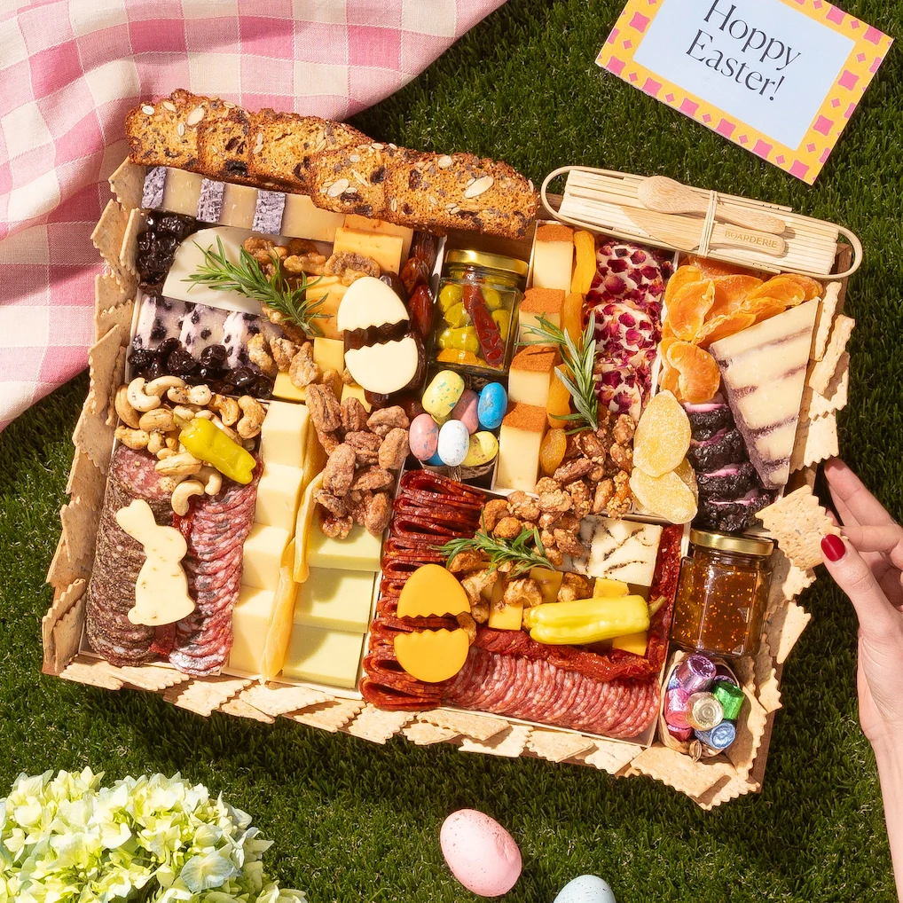 Boarderie large Easter charcuterie board with artisan cheeses, meats, Easter egg candies and spring details on a wooden serving tray