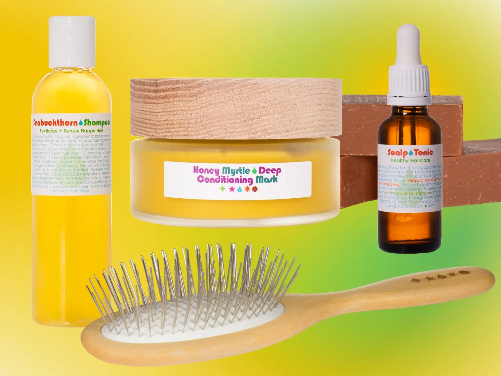Living Libations botanical hair care collection with seabuckthorn shampoo in bright yellow, conditioner mask (flat glass yar also bright yellow contents), scalp tonic (brown dropper bottle), beechwood brush, and pink clay soap (stacked in the background), background is a gradient of different colors